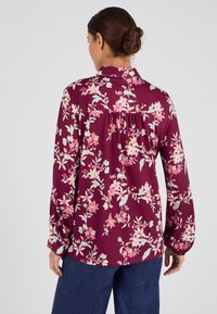 Camisa de manga larga burdeos con un estampado floral en rosa y verde. Presenta un cuello y puños abotonados. Tela suave con un ajuste relajado.