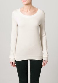 Maglione lungo color beige chiaro con maniche lunghe e scollatura rotonda, realizzato in tessuto morbido, presenta polsini a costine e un design slim-fit.