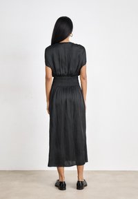 Robe midi noire avec une coupe décontractée, une taille smockée et des manches courtes. Tissu lisse et design longueur cheville. Portée avec des chaussures de ville noires.
