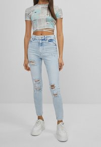 Ljusblå, hög midja skinny jeans med slitna detaljer och hål. Kombination med en kort, grafisk t-shirt och vita sneakers.