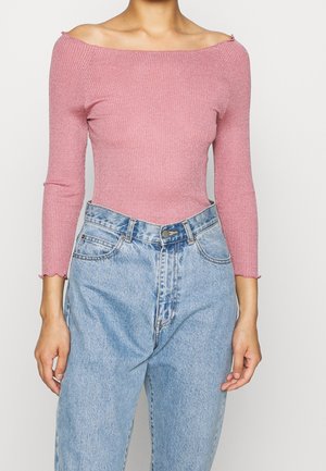 Femme portant un haut côtelé rose à épaules dénudées avec des manches trois-quarts et un jean en denim bleu clair taille haute.