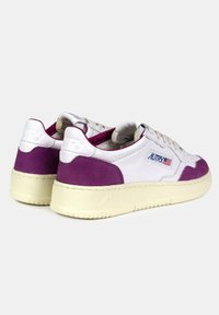 Sneakers bianchi e viola con tomaia texturizzata, dettagli in suede e un logo prominente. Presentano una suola in gomma e lacci piatti.