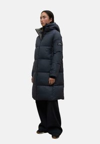 Abrigo parka acolchado de color azul marino oscuro con capucha, que cuenta con un forro gris en contraste, una silueta larga y patrones cuadraditos cosidos.