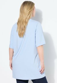 Světle modré oversized tričko s krátkým rukávem, vyrobené z měkké látky, s kulatým výstřihem a rovnými lemy, v kombinaci s tmavými džínami.