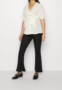 Blusa crema chiaro con pois neri, fiocco in vita, maniche a palloncino corte, abbinata a pantaloni neri a palazzo e mocassini lucidi.