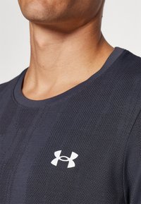 Sötétkék sport póló, textúrált mintázattal, kerek nyakkal és fehér Under Armour logóval a mellkas bal oldalán.