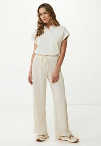 Vit bomullspolo med subtil brodyr, i kombination med strukturerade beige vida byxor och beige sportiga sneakers.