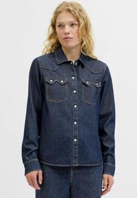 Temno moder jeans srajca z dolgimi rokavi, zapiranje na snaps gumb, koničast ovratnik in dvojna prsna žepa. Ima vidne šive.