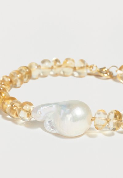 Βραχιόλι με διαφανείς κεχριμπαρένιες χάντρες και μια μεγάλη ακανόνιστη λευκή πέρλα στο κέντρο, τοποθετημένο πάνω σε απλό ανοιχτό φόντο.