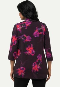 Blumen-Tunika mit Drei-Viertel-Ärmeln, die einen dunkelpurpurfarbenen Grund und lebhafte rosa und orangefarbene Blumenmuster aufweist. Weicher, leichter Stoff.