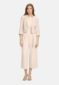 Beige cropped blazer gecombineerd met een bijpassende jumpsuit met wijde benen, voorzien van een geknoopte taille en korte mouwen. Gladde stof en minimalistisch ontwerp.