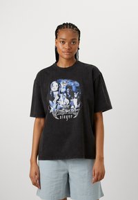 Black oversized T-shirt made of cotton featuring a graphic print with characters and text, set against a faded background. Short sleeves.