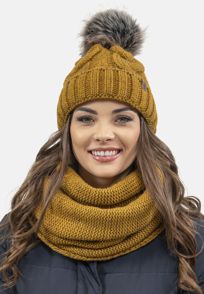 Căciulă galbenă tricotată cu un model texturat și un pom-pom din blană sintetică, asociată cu o fulară groasă tricotată în aceeași nuanță.
