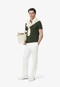 Polo verde con colletto bianco, maglione crema drappeggiato sulle spalle, pantaloni bianchi e sneakers bianche con accenti verdi.