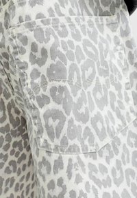 Gros plan d'un tissu à imprimé léopard gris et blanc avec une poche appliquée cousue, partie d'un vêtement.