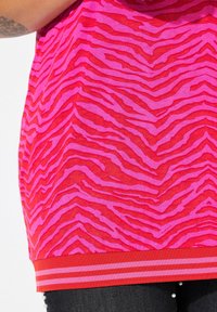 Tričko s krátkým rukávem v jasně růžové barvě s červeným zebra vzorem. Má jednobarevný červený lem se dvěma růžovými pruhy. Lehký materiál.