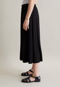 Sort ankel-længde nederdel med en samlet elastisk talje, parret med sorte, laklæder sandaler med spænde og åben design.