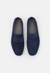 Mocassins en suede bleu marine avec une finition lisse, des détails de couture et une couture surélevée sur l'empeigne. L'intérieur présente une doublure grise avec un logo.