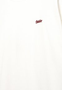 Cremefarvet t-shirt lavet af bomuld, med et lille broderet logo i maroon på den øverste venstre brystområde. Korte ærmer, standard pasform.