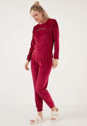 Red velvet pajama set featuring long sleeves and elastic waistband pants. Script text on the top; soft texture; paired with fluffy slippers.