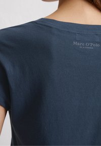 Marinblå bomullströja med rund halsringning, korta ärmar och en subtil logotryck på baksidan. Strukturerad, ribbad tyg.