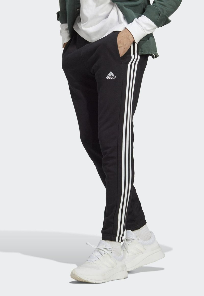 Fekete zsákos nadrág fehér háromcsíkos díszítéssel és Adidas logóval, puha anyagból készült, slim fit szabású, oldalsó zsebekkel.