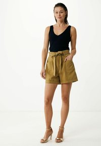 Schwarzes geripptes Tanktop kombiniert mit khakifarbenen, hoch taillierten Shorts mit einem gebundenen Gürtel, seitlichen Taschen und einem glatten Stoff. Goldene Absatzsandalen.