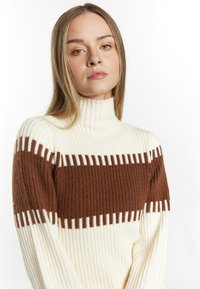 Maglione a collo alto a coste in crema e marrone. Presenta righe orizzontali e una silhouette aderente. Texture morbida con un colletto alto.