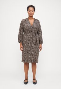 Robe à imprimé léopard en matériau l�éger, longueur genoux avec un design enveloppant, décolleté en V et manches longues bouffantes. Associée à des chaussures plates noires.