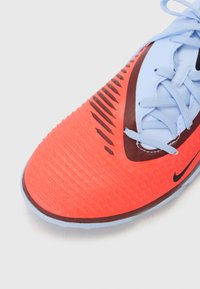 Nike jalatsid, millel on oranž tekstureeritud ülemine osa, must swoosh logo ja helesinised paelad ja detailid. Omab voolavat disaini ja soonelist pinda.