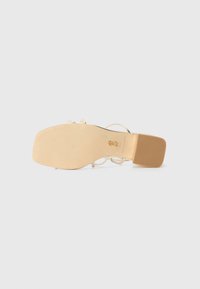 Beige gestützte Sandale mit glattem, braunem Fußbett, transparenten Riemen und quadratischer Zehenpartie. Goldene Akzente an dem Riemen mit strukturiertem Griff auf der Sohle.