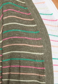 Sweter z dzianiny w kolorze oliwkowym, z poziomymi paskami w różowym, białym i turkusowym. Posiada teksturowe wykończenie oraz dekolt w kształcie litery V.