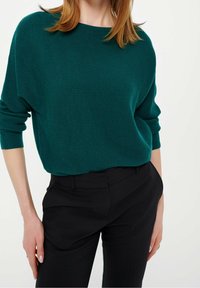 Teal geribbelde trui met een brede halslijn en lange mouwen, gecombineerd met zwarte gep tailored pants; zachte textuur en ontspannen pasvorm.