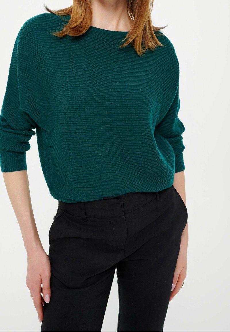 Teal geribbelde trui met een brede halslijn en lange mouwen, gecombineerd met zwarte gep tailored pants; zachte textuur en ontspannen pasvorm.