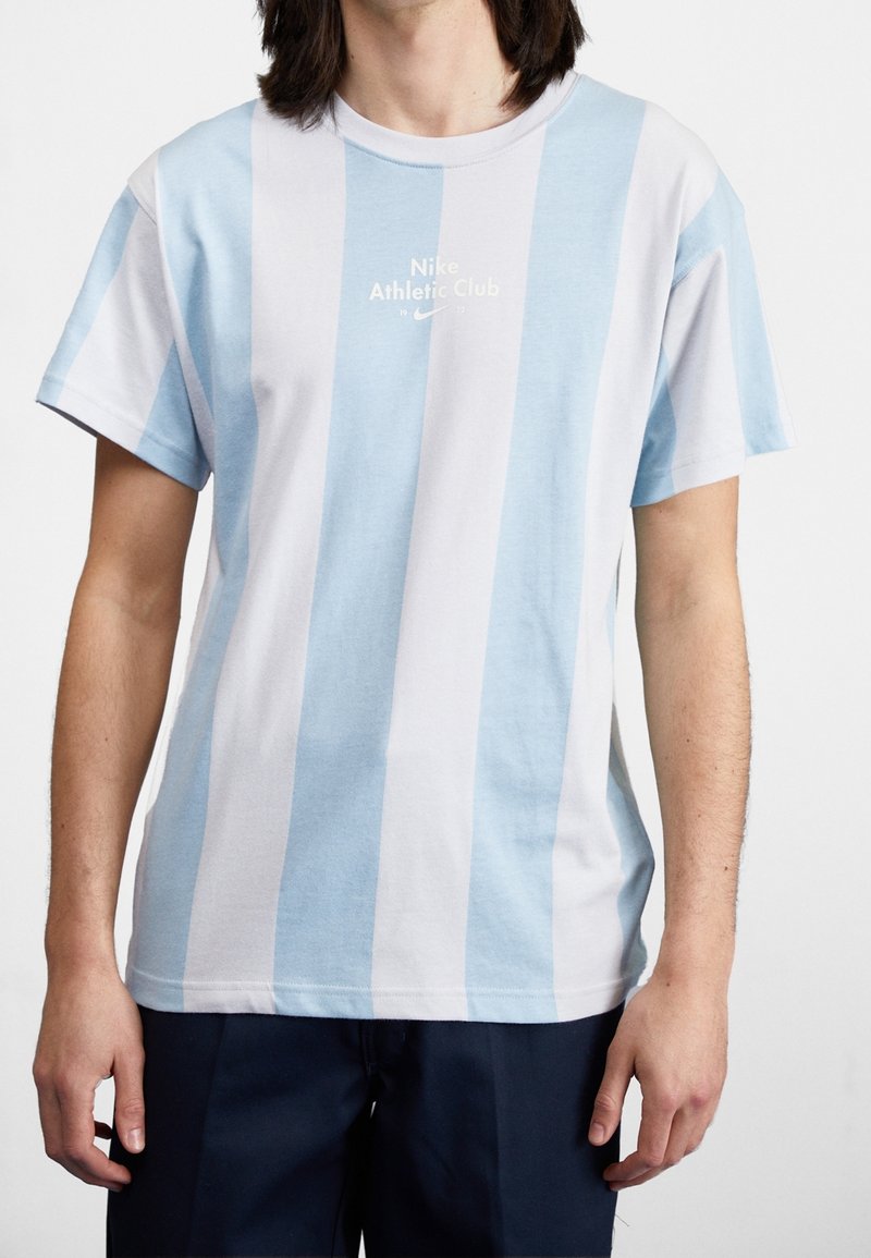 Světle modré a bílé pruhované bavlněné tričko s kulatým výstřihem a logem "Nike Athletic Club" uprostřed. Krátké rukávy, volný střih.