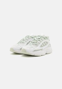 Vita nät sneakers med mintgröna accenter, som har en tjock sula, snörningsdesign och texturerade mönster på överdelen.