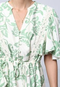 Robe blanche avec un motif floral vert, dotée d'un décolleté en V, d'une finition en dentelle sur les manches et d'une taille cintrée avec un détail à cordon.