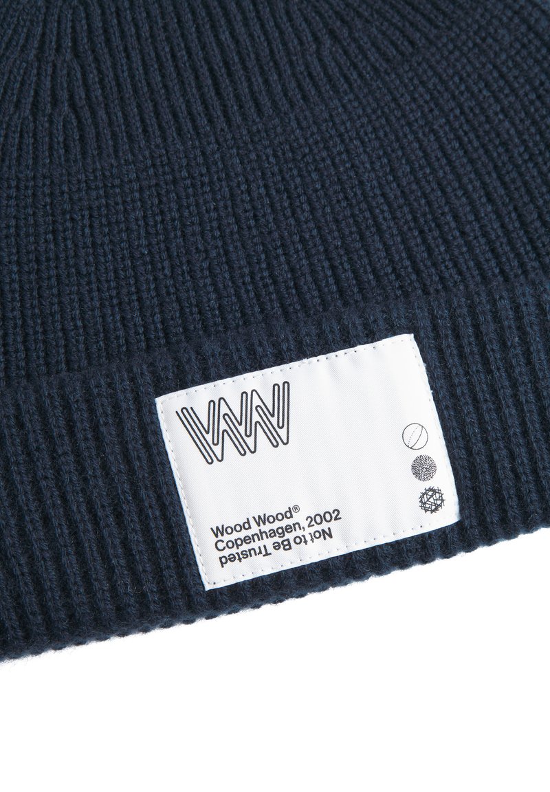 Navy ribbed knit beanie made of wool. Features a white label with logo and care symbols. Soft texture with elastic shape for fit.