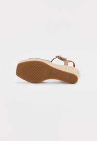 Sandale compensée marron avec un fond texturé de style espadrille, dotée d'une bride réglable avec un accent métallique et d'un design perforé sur la semelle.
