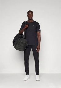 Čierne športové tričko s logom, v kombinácii s čiernymi zúženými nohavicami a bielymi teniskami. Nosená veľká čierna športová taška.