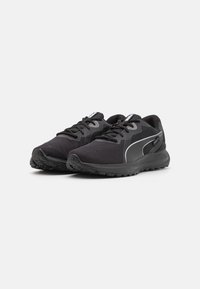 Zapatillas deportivas negras con parte superior de malla, suela de goma gruesa y acentos reflectantes en los lados. Cuenta con cordones y cuello acolchado.