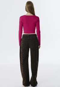 Top long à manches longues rose côtelé ajusté associé à un pantalon large à motif léopard brun, mettant en valeur la texture et les couleurs contrastées.
