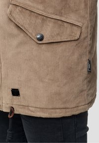 Kordjacke in Hellbraun mit gerippter Textur, ausgestattet mit Druckknopfverschluss, Brusttasche und Kordelzug am Saum.