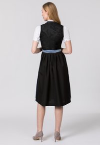 Traditionelles Kleid mit einer schwarzen Weste mit floralen Mustern, weißer Bluse und einem blauen Band in der Taille. Der Rock ist plissiert, knielang und aus schwarzem Stoff.