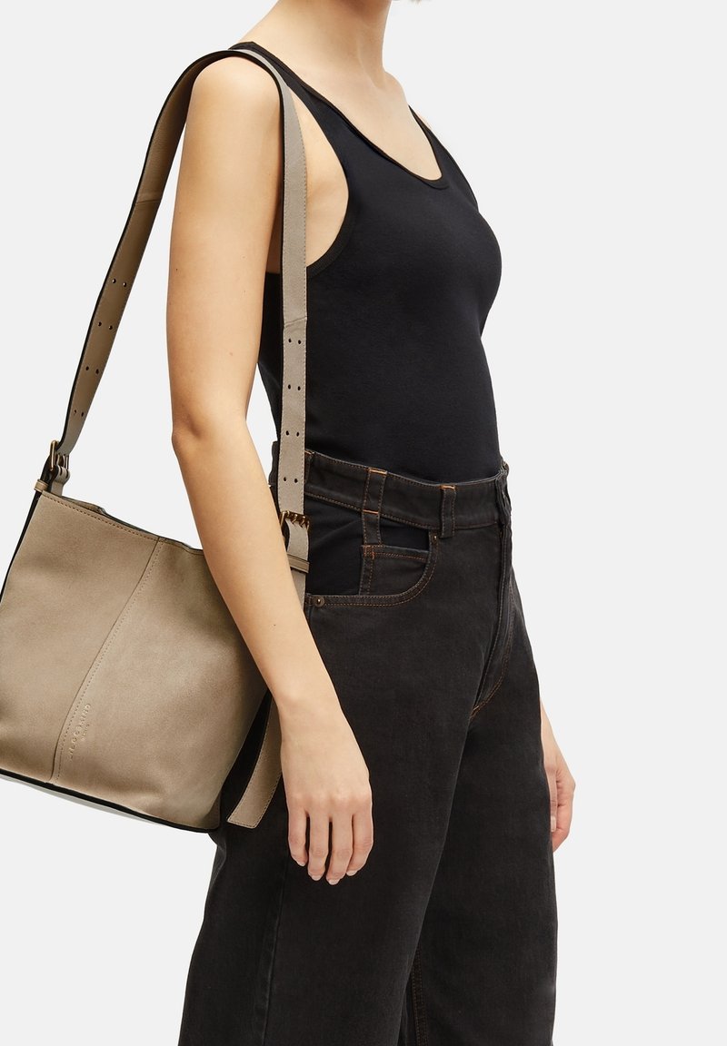 Borsa a tracolla in pelle beige con tracolla regolabile, design bicolore e texture liscia, abbinata a un top fitted nero e jeans scuri.