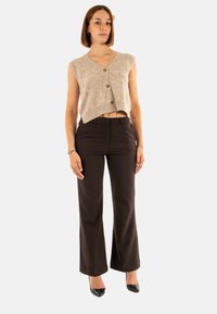 Top corto in maglia beige senza maniche con chiusura a bottoni, abbinato a pantaloni aderenti marrone scuro e décolleté nere a punta.