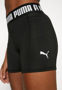 Gros plan sur un short de sport noir Puma avec le logo Puma blanc sur la cuisse et une ceinture marquée à la taille et aux jambes supérieures d'une personne.