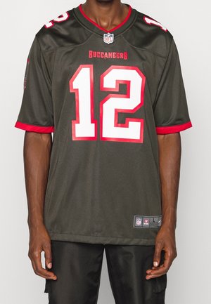 Mężczyzna noszący ciemnozieloną koszulkę futbolową Tampa Bay Buccaneers z czerwonymi wykończeniami i numerem 12 w białym i czerwonym kolorze z przodu.