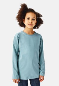 Langærmet t-shirt i lyseblå, lavet af blød bomuld. Har rund halsudskæring og enkelt design, kombineret med mørke jeans.