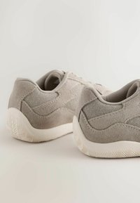 Baskets grises en daim avec une finition texturée, dotées d'une semelle en caoutchouc blanche et de détails cousus sur la tige. Vue des talons.